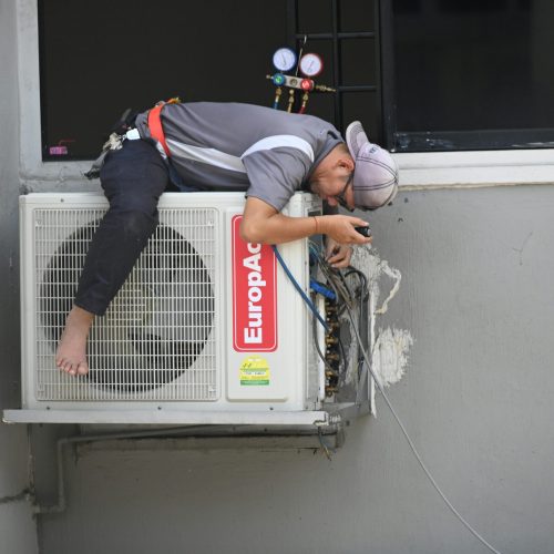 A technician skillfully repairing an outdoor air conditioning unit mounted on a building wall.